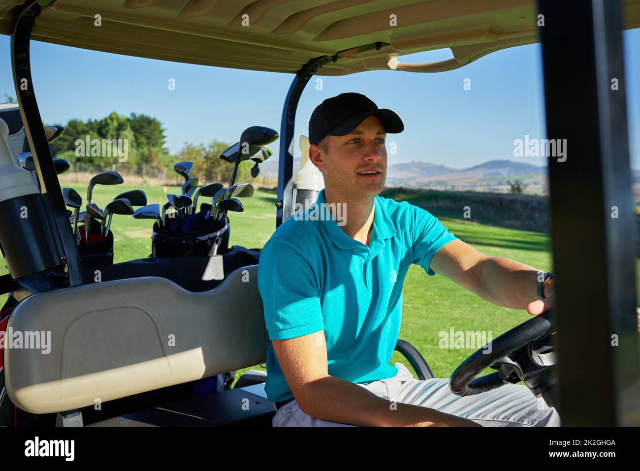 Andando al buco seguente. Scatto di un giovane uomo allegro che guida in un golf cart al buco seguente su un campo da golf. Foto Stock