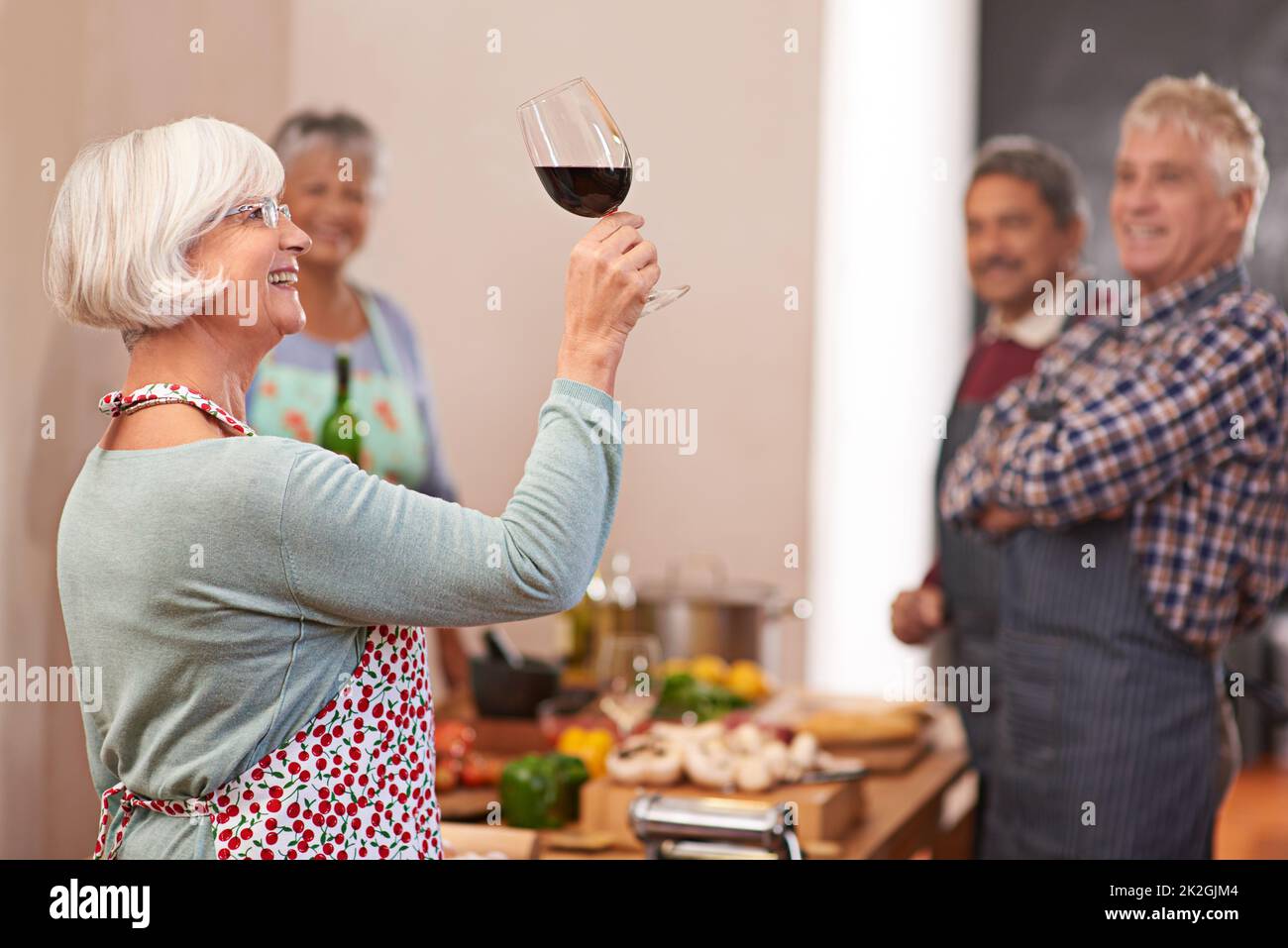 Serve sempre le annate migliori. Scatto di una donna anziana che guarda il suo vino con gli amici sullo sfondo. Foto Stock