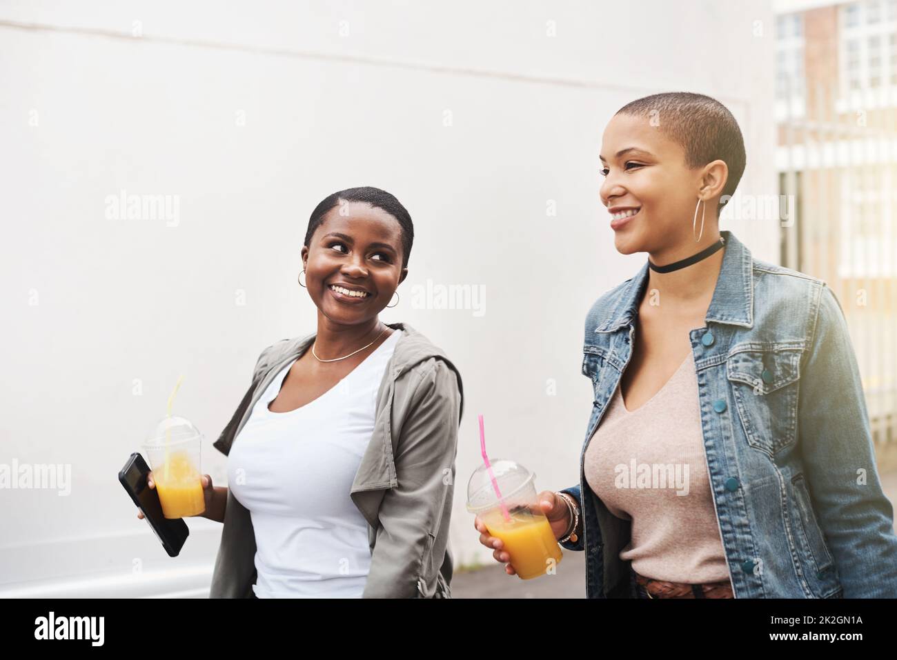 Insieme attraverso spesso e sottile. Scatto di due giovani donne che camminano in città ridendo mentre tengono le loro bevande fredde. Foto Stock