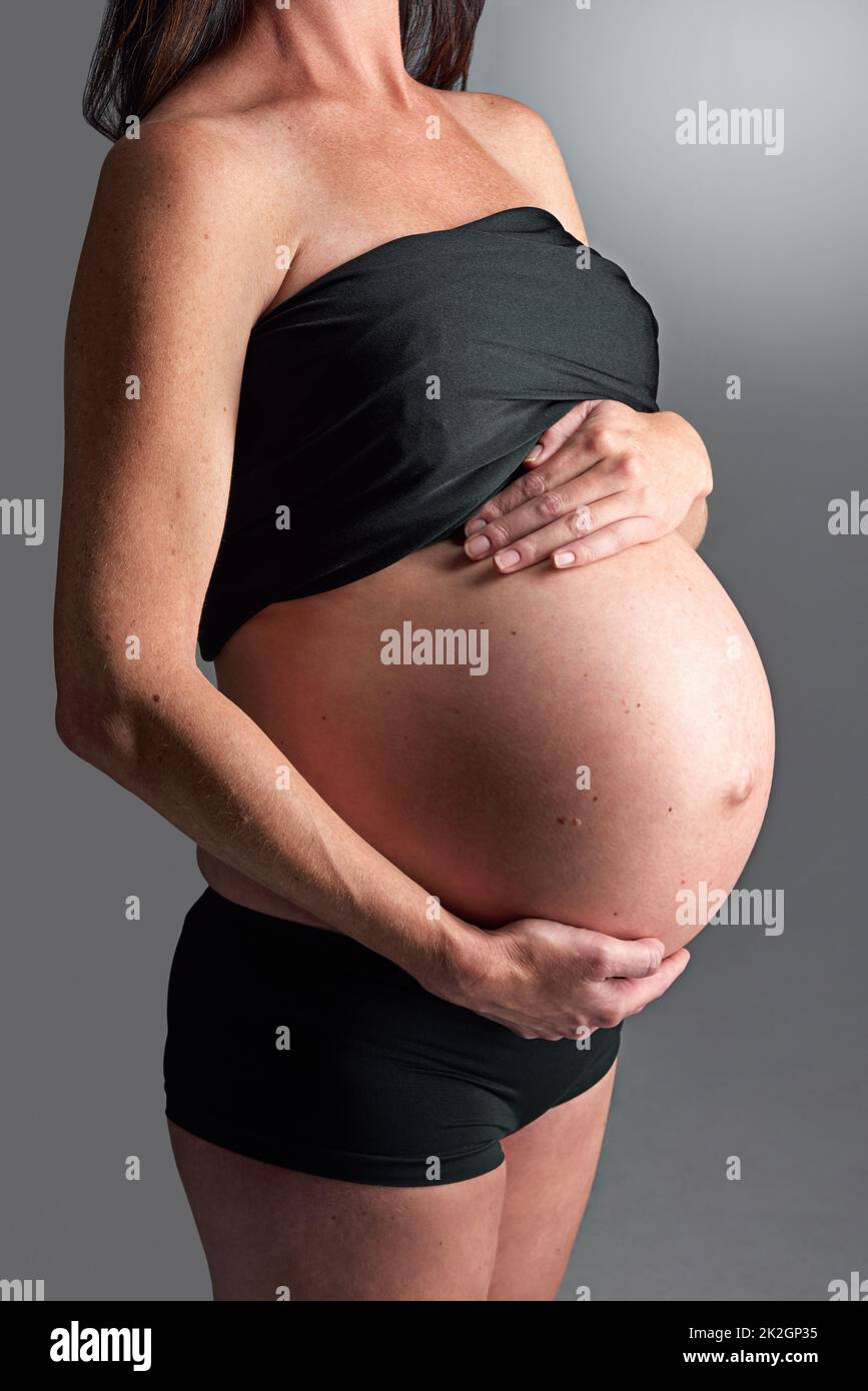 Aspettandosi il suo arrivo presto. Una donna incinta che tiene la pancia. Foto Stock