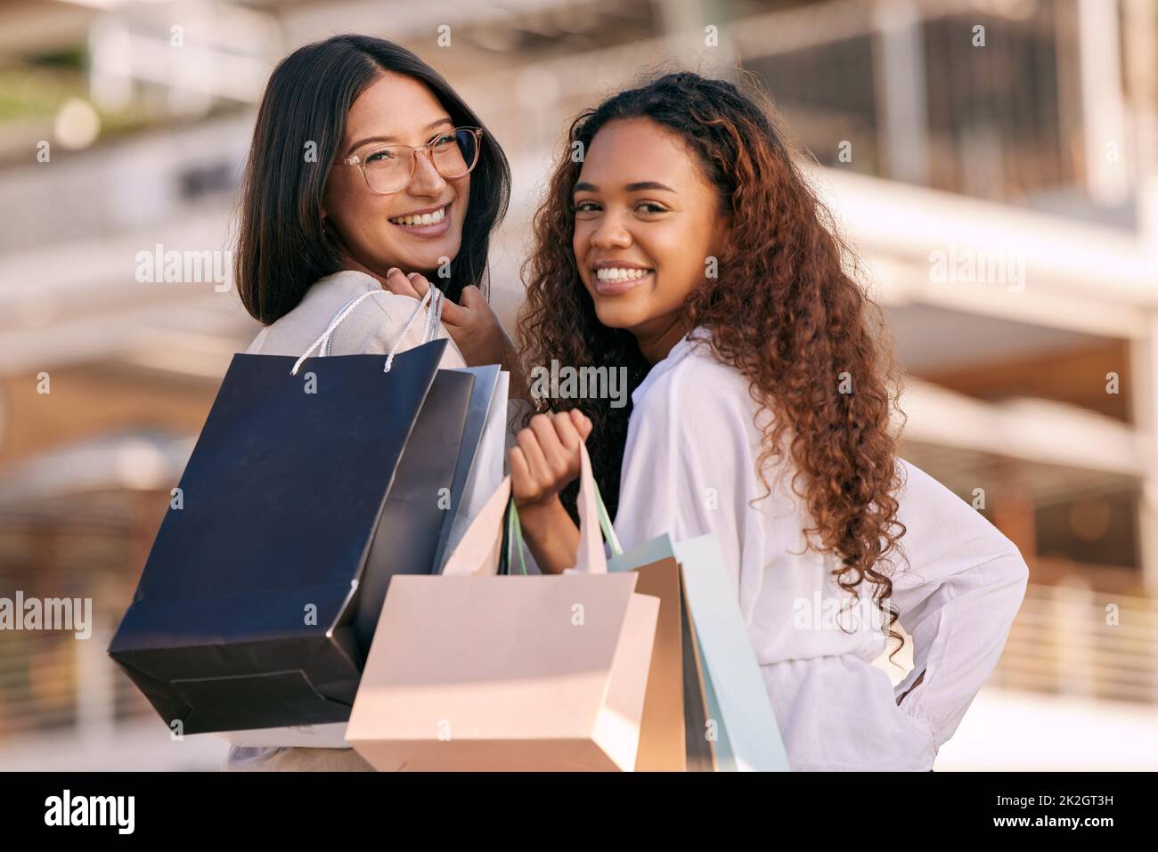 Terapia di incollaggio e vendita al dettaglio. Foto di due giovani donne attraenti che si levano in piedi fuori insieme e che si legano mentre fanno shopping in città. Foto Stock