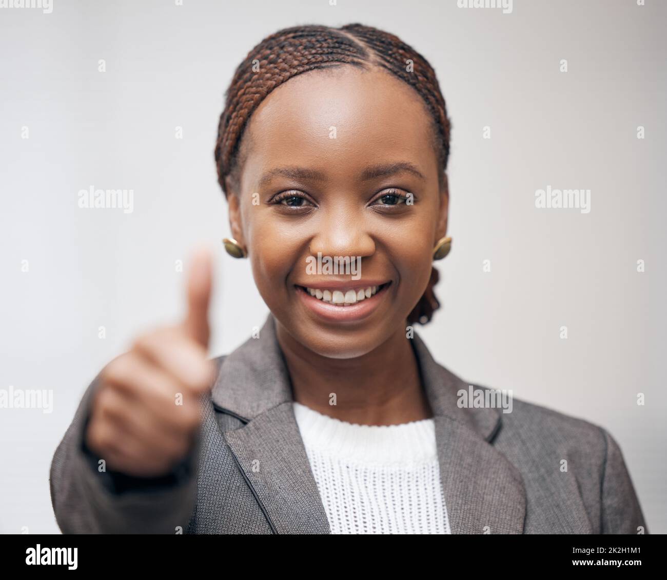 Io credo in te. Ritratto di una giovane donna d'affari che mostra i pollici su uno sfondo grigio. Foto Stock