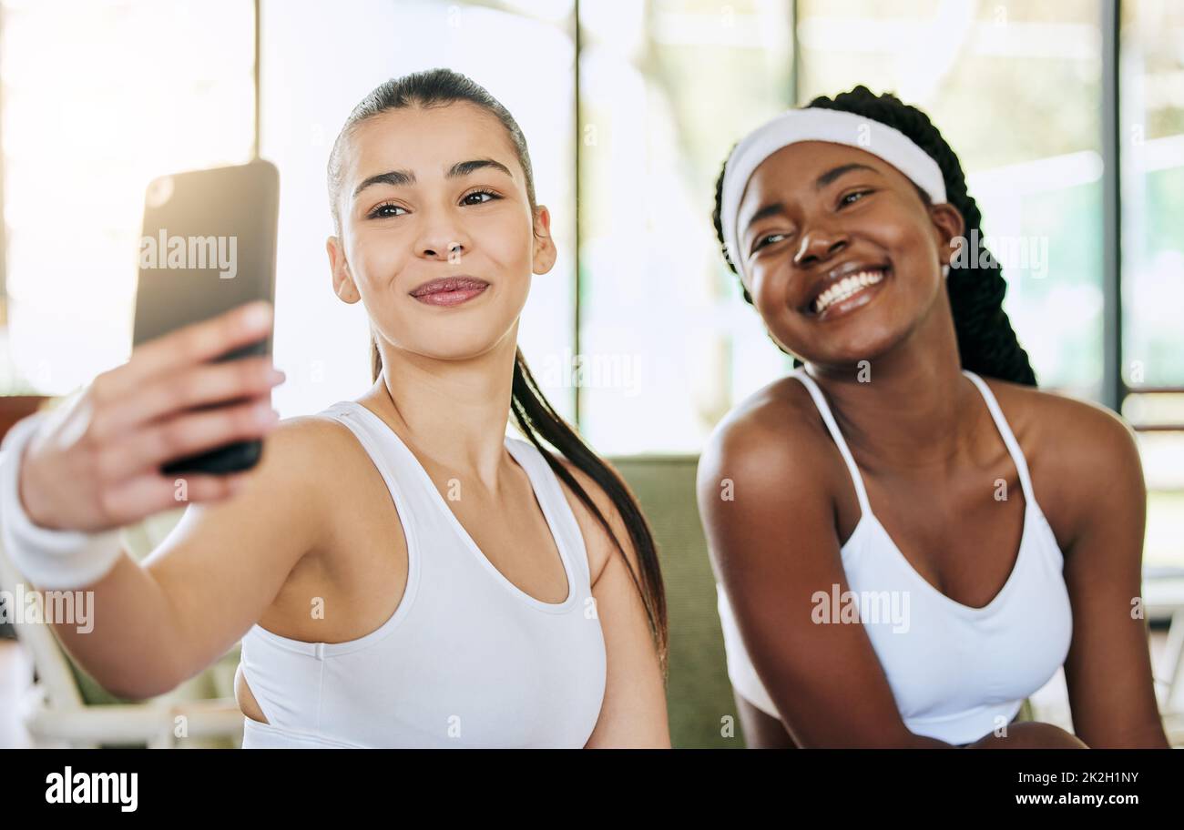 Bene prenda un altro dopo che raccogliamo il nostro trofeo. Scatto corto di due giovani giocatori di tennis femminile attraenti che prendono selfie nella loro clubhouse. Foto Stock