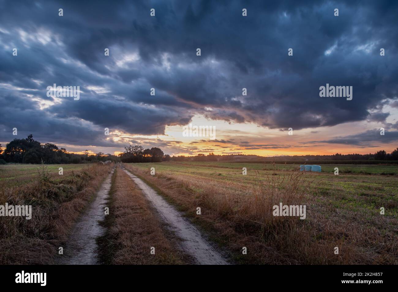 Strada sterrata attraverso il campo e nuvole dopo il tramonto Foto Stock