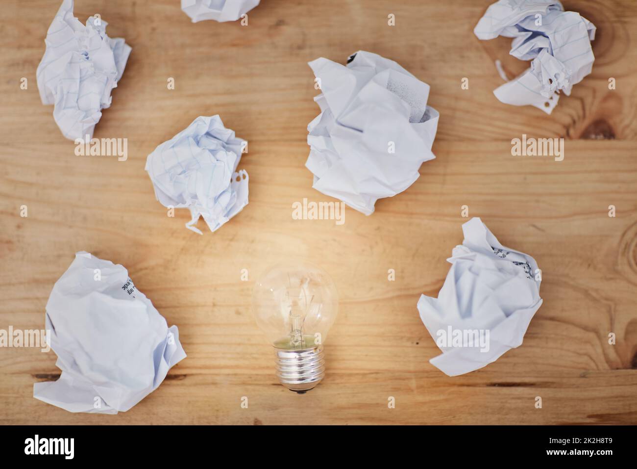 Blocco scrittori. Scatto ad alta angolazione di una lampadina circondata da pezzi di carta sgualciti su una scrivania. Foto Stock