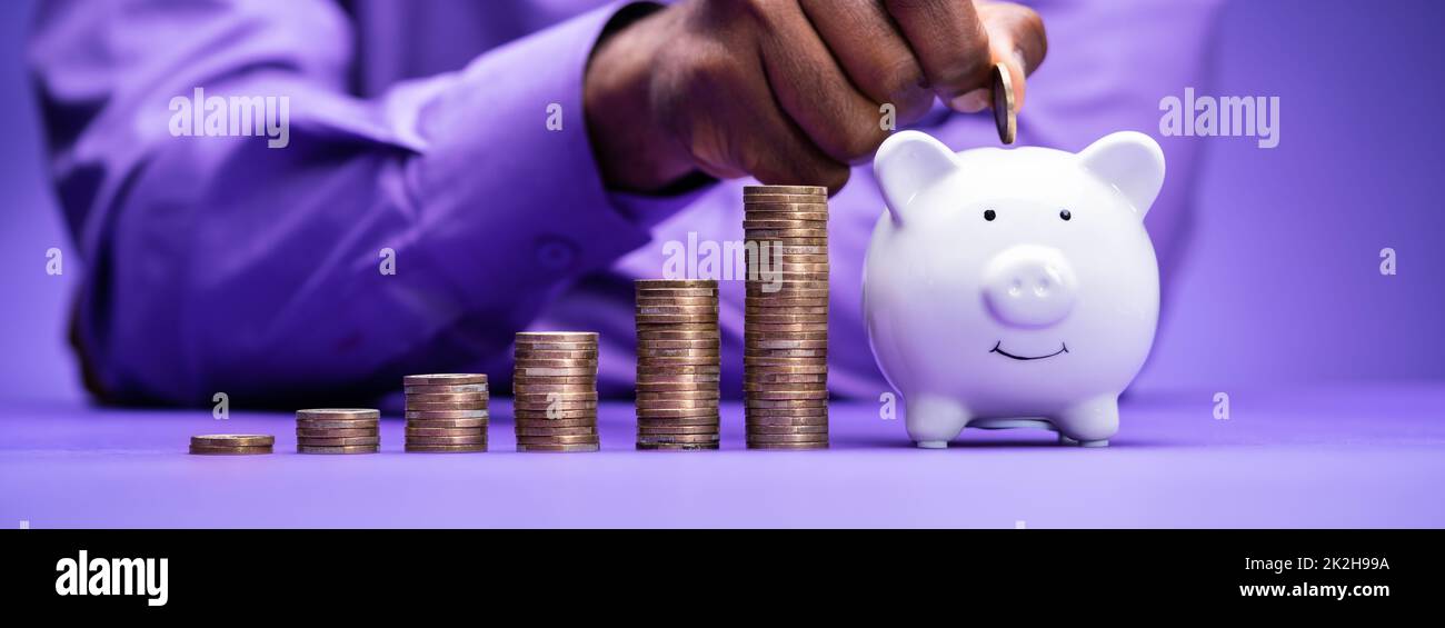 Inserimento di moneta nel Piggybank con crescente pila di monete Foto Stock