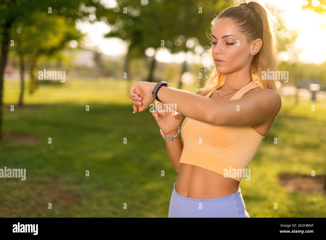 Primo piano ripresa di una donna con tights blu che guarda il suo orologio intelligente in un parco pubblico al mattino Foto Stock