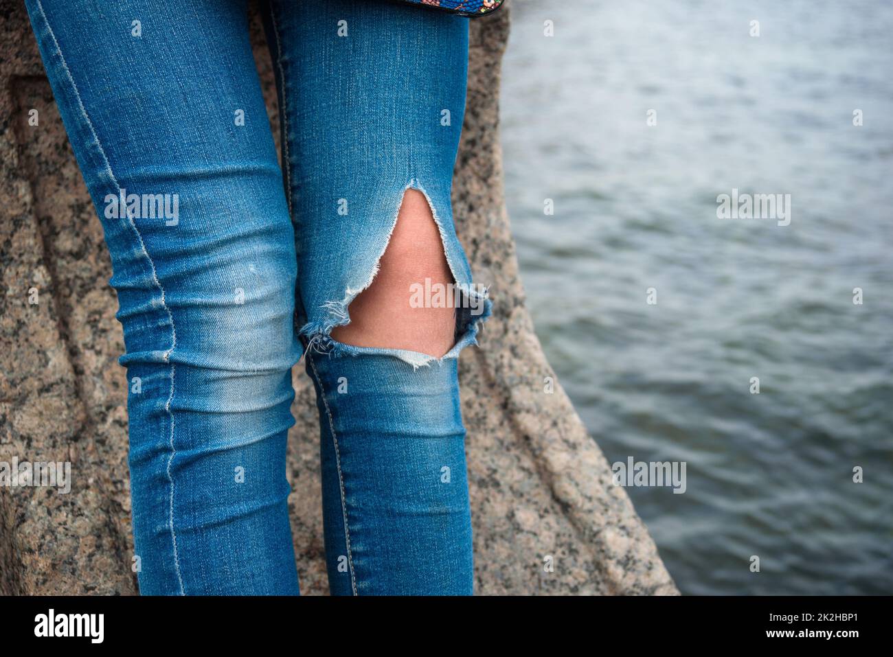 Gambe di donna in jeans strappati sul ginocchio siede sul molo contro l'acqua Foto Stock
