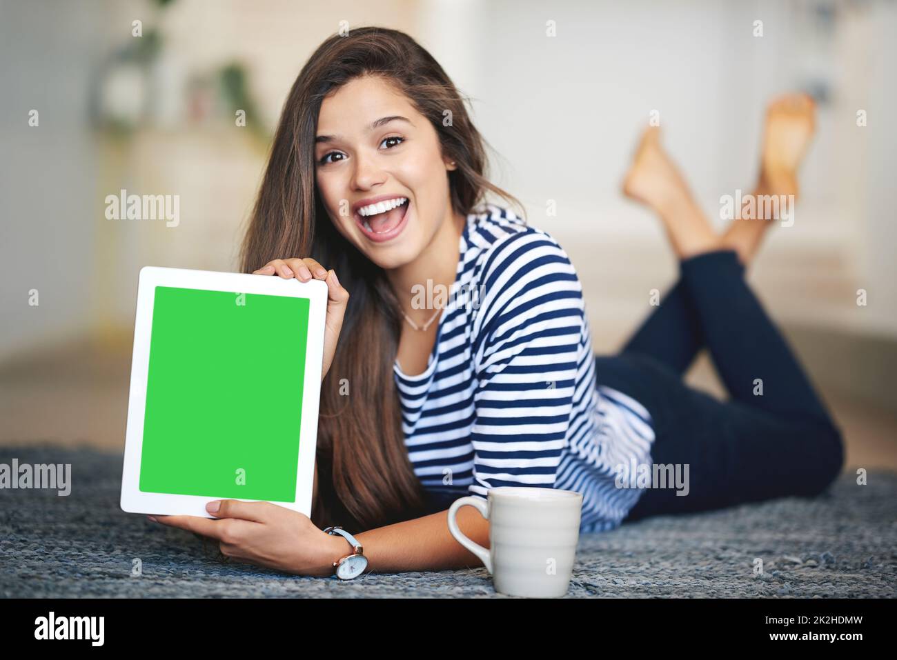 Questo è un sito che youre andare a visitare. Ritratto di una giovane donna estatica sdraiata sul pavimento a casa con un tablet digitale dotato di schermo con tasti croma. Foto Stock
