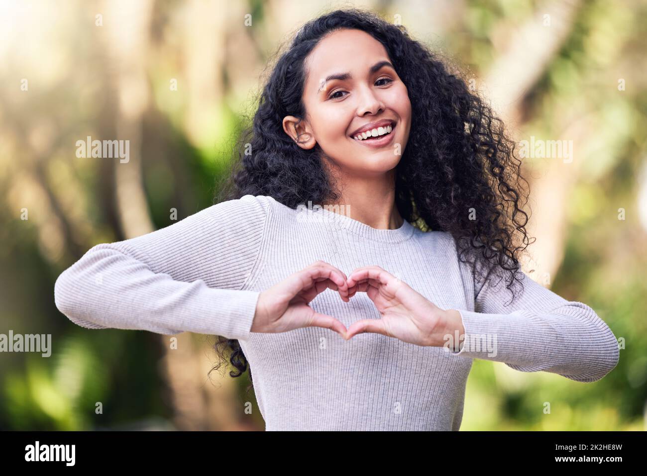 Ti amo, mi ha detto il cuore. Scatto di una giovane donna che fa un gesto a forma di cuore mentre si gode una giornata fuori nella natura. Foto Stock