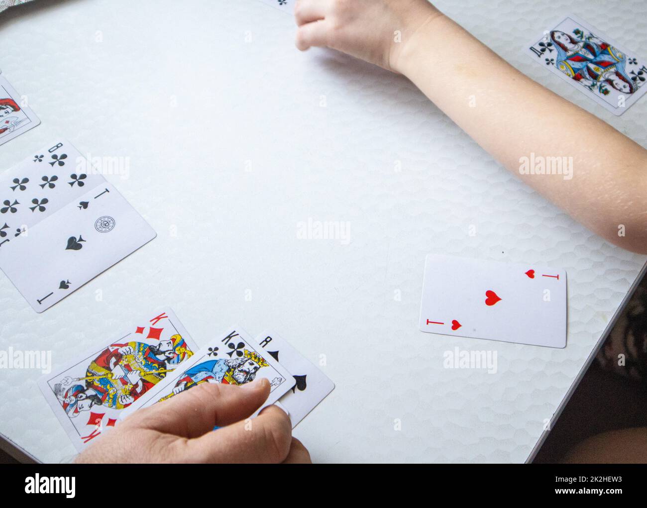 Primo piano della mano di un uomo e della mano di un bambino che stende le carte da gioco su un tavolo bianco, il concetto di imparare a giocare le carte Foto Stock