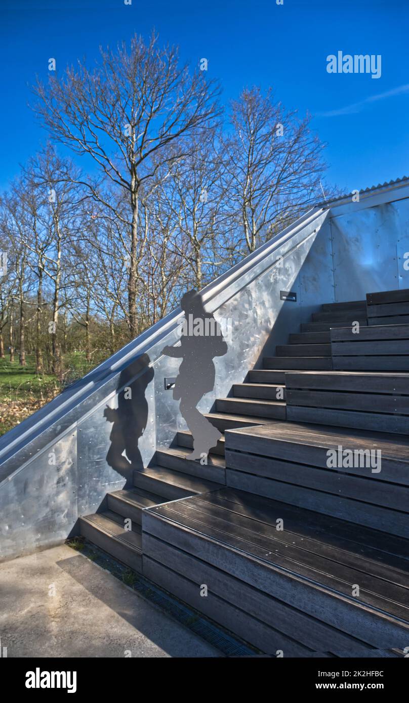 giovane donna sconosciuta e la sua ombra camminando giù scale di legno (costruzione di metall) in un'area di svago all'aperto, tempo luminoso e cielo blu, elaborato digitalmente Foto Stock