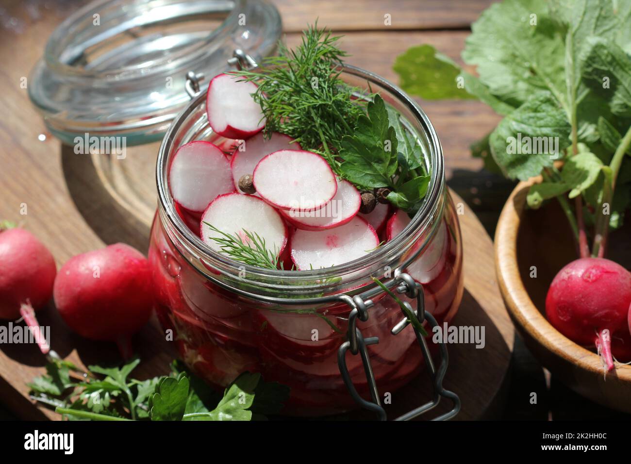 Vasetto di vetro in vetro decapato di ravanello rosso su un tavolo di legno. Conserve di verdure fermentate. Foto Stock