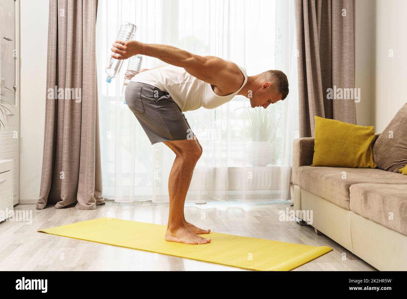 Giovane uomo atletico che usa bottiglie d'acqua per l'allenamento domestico Foto Stock