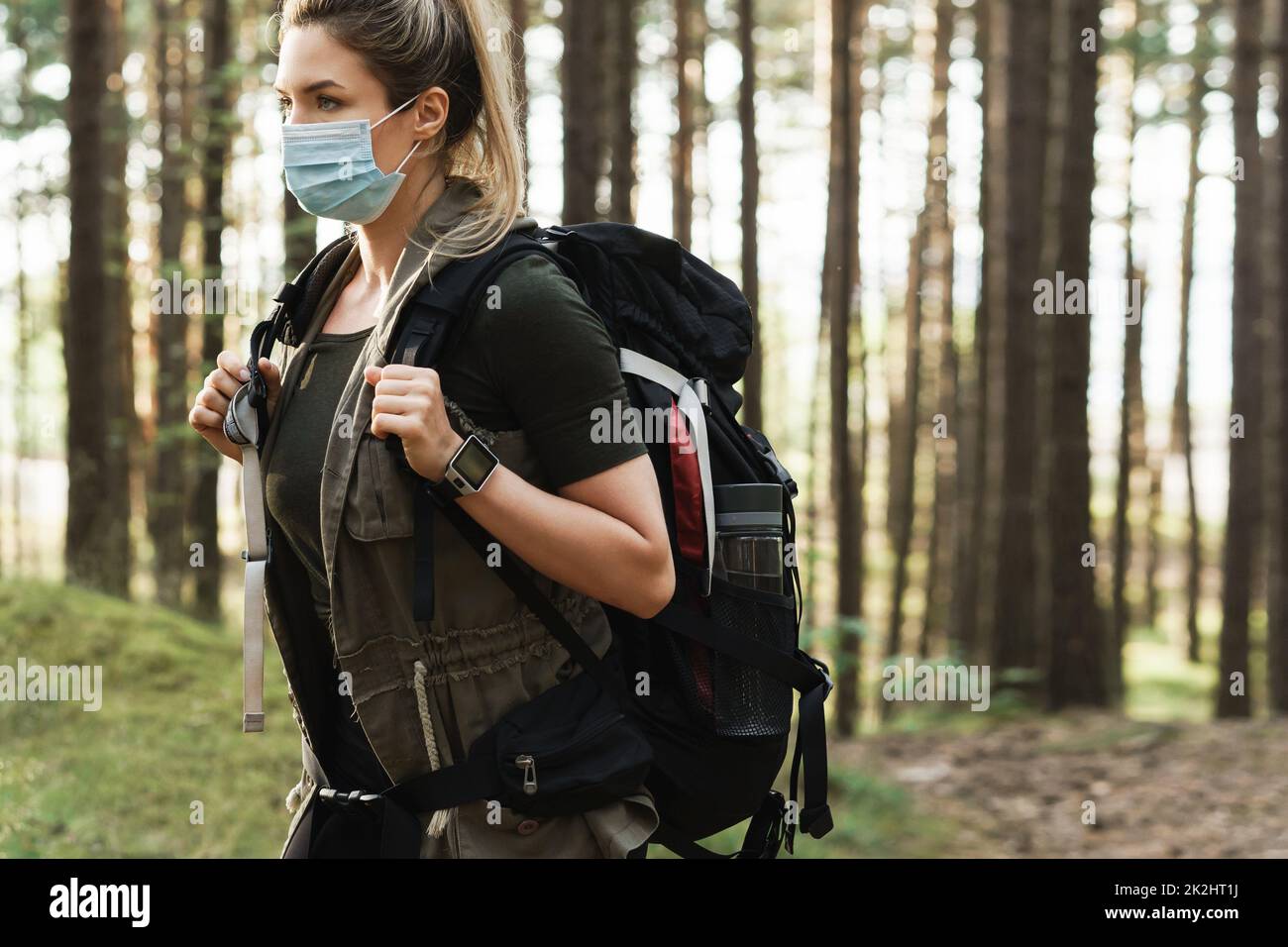 Donna escursionista con uno zaino indossare maschera di prevenzione durante la sua escursione nella foresta Foto Stock