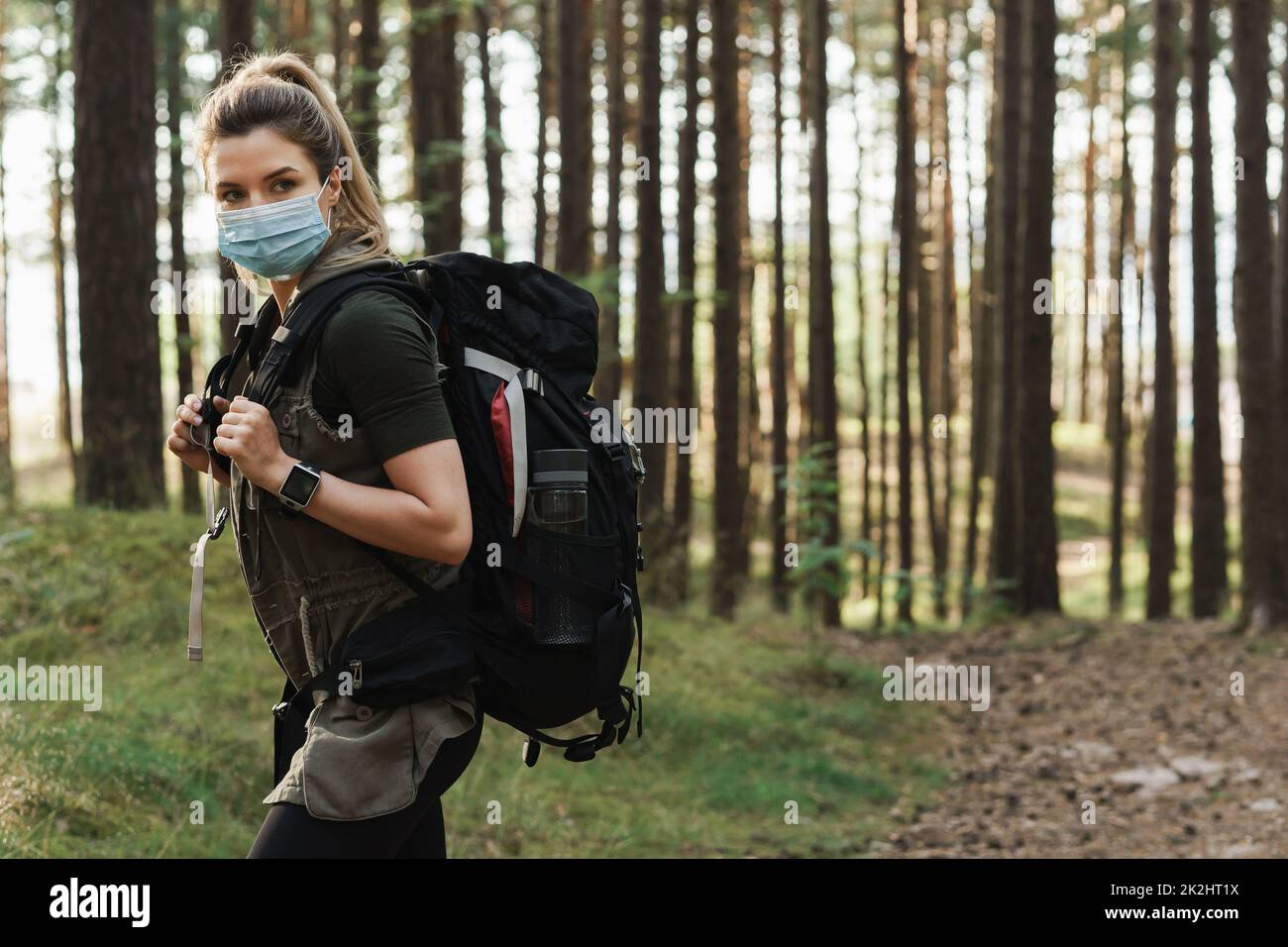 Donna escursionista con uno zaino indossare maschera di prevenzione durante la sua escursione nella foresta Foto Stock