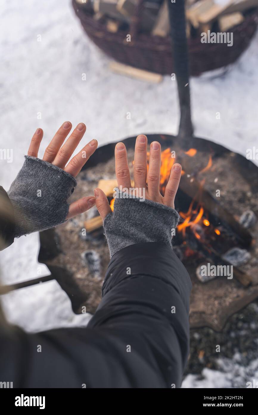 Donna che scalda le mani dalla fossa del fuoco Foto Stock