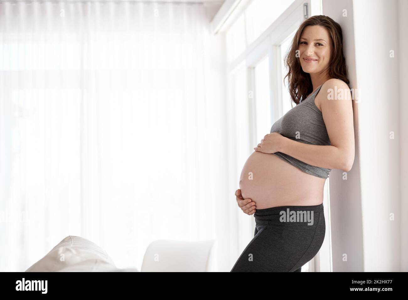 Irradiando con istinti materni. Ritratto corto di una giovane donna incinta in piedi nella sua casa. Foto Stock
