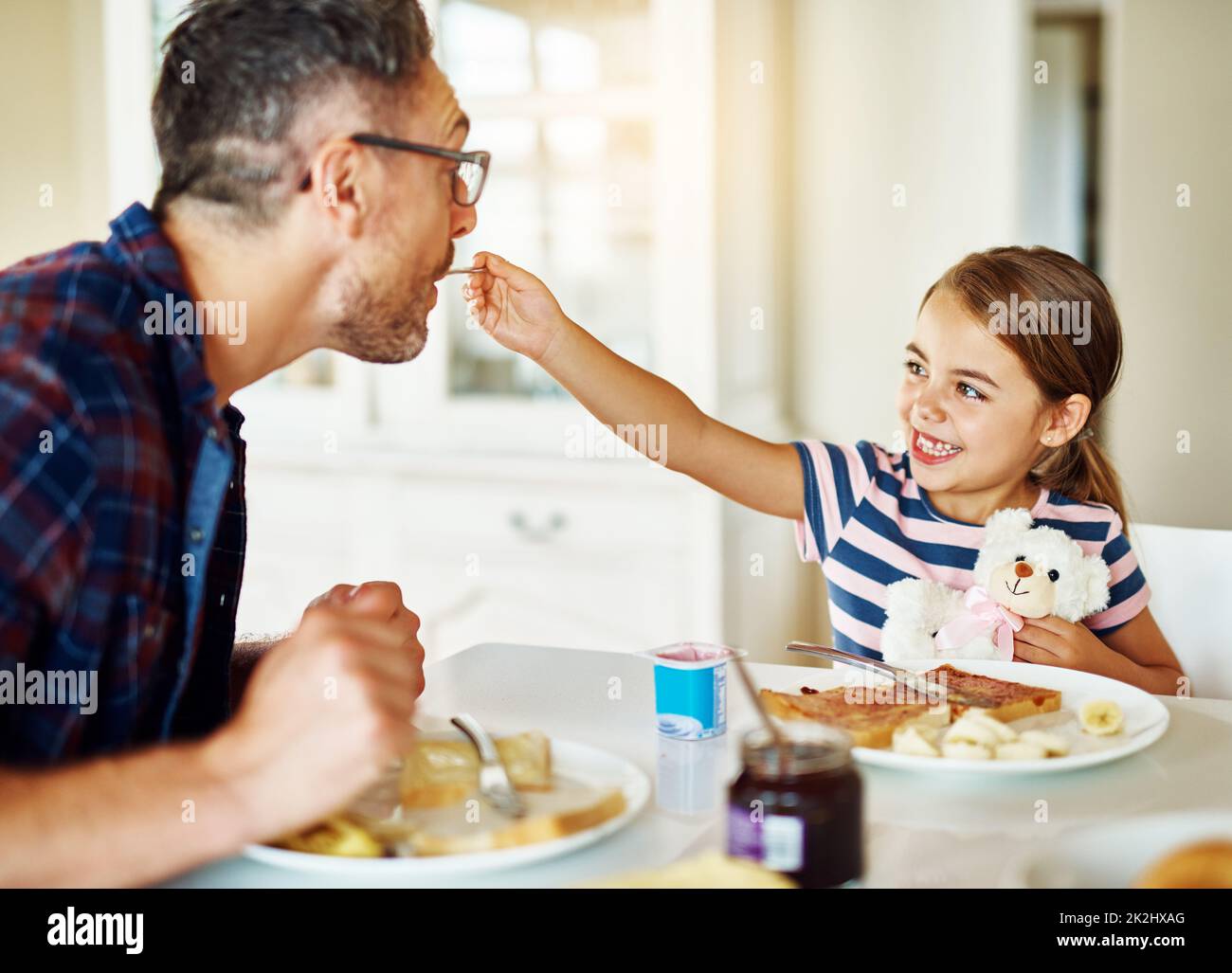 Assaggia il mio. Scatto corto di una bambina adorabile che ha fatto colazione con suo padre in cucina. Foto Stock