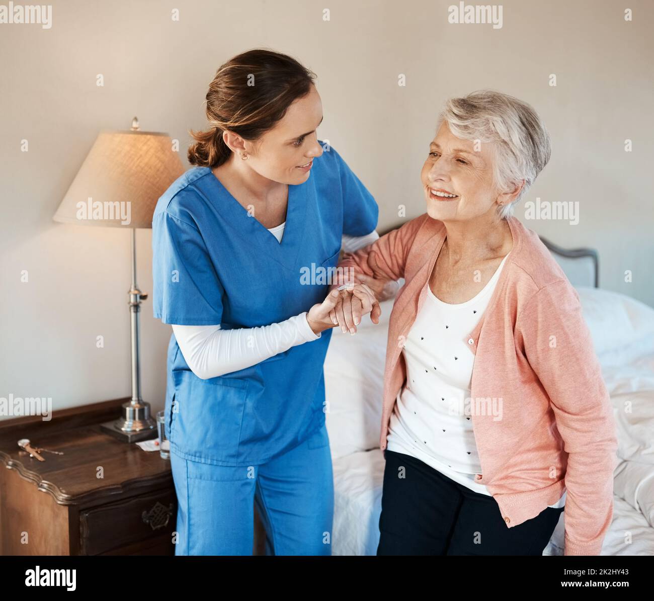 Sono pronto per una giornata fuori. Shot di una giovane infermiera che aiuta una donna anziana ad alzarsi dal letto in una casa di cura. Foto Stock