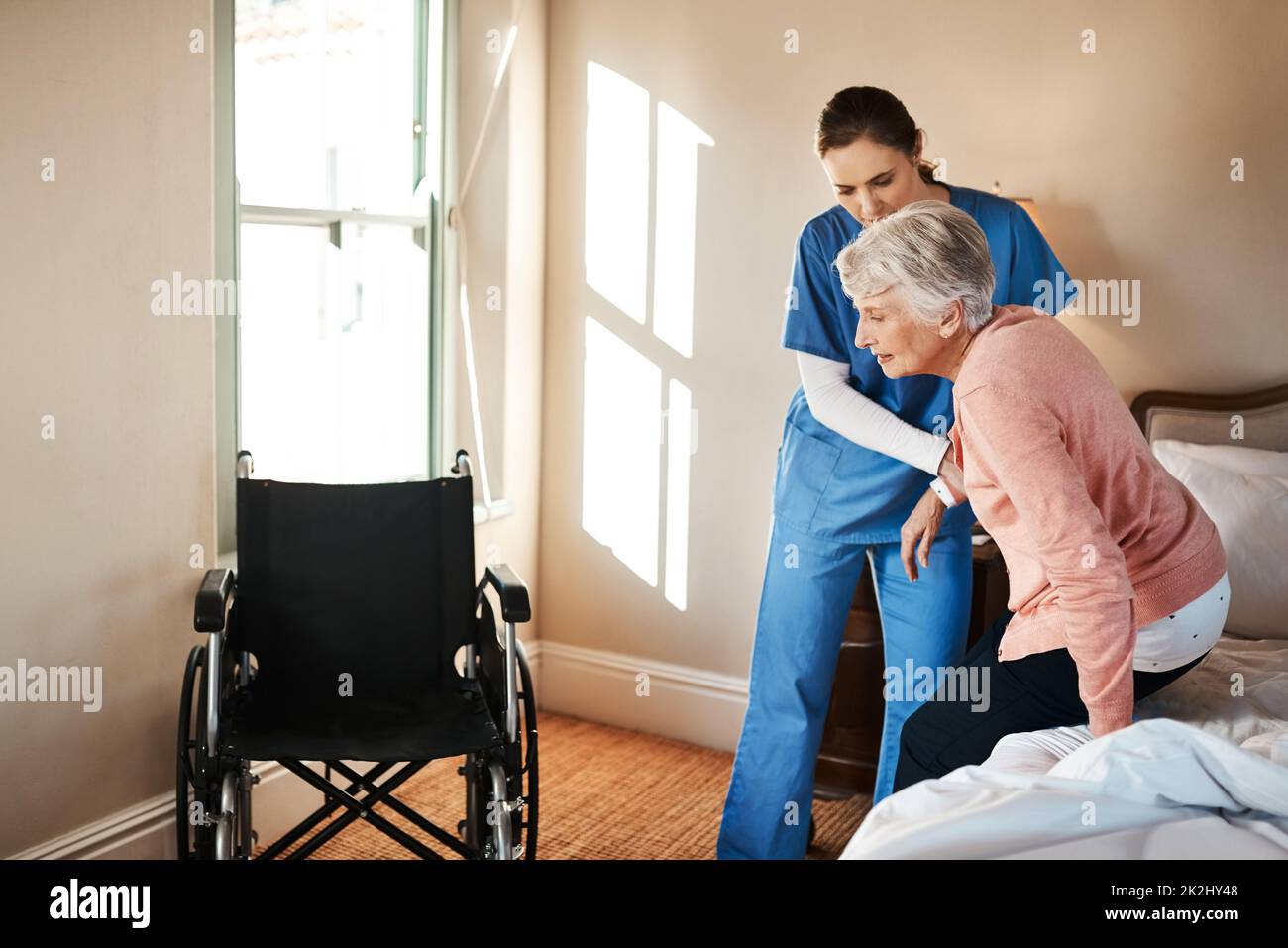 I movimenti semplici non sono più così semplici. Shot di una giovane infermiera che aiuta una donna anziana ad alzarsi dal letto in una casa di cura. Foto Stock