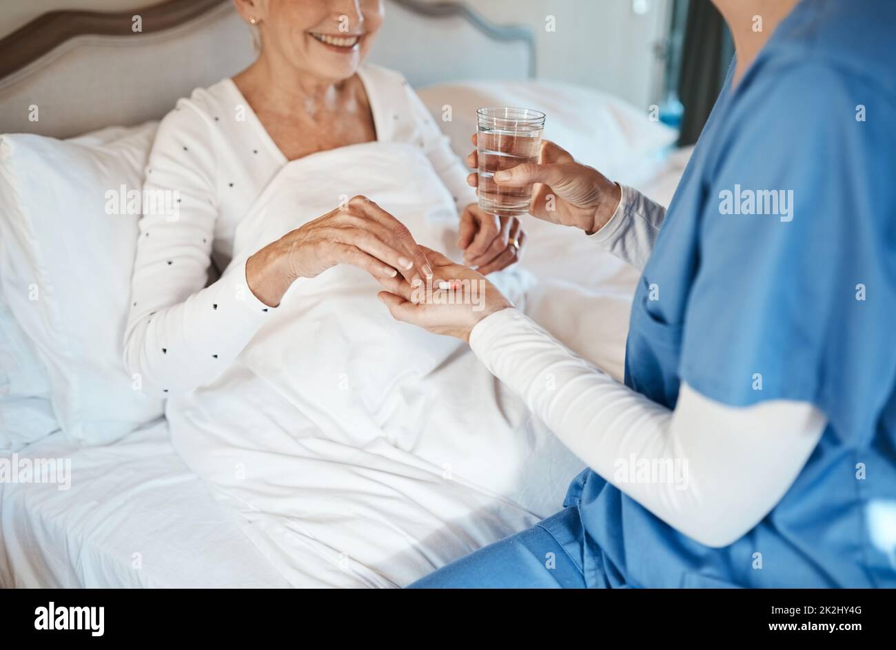 Un trattamento affidabile è nelle sue mani. Shot di un'infermiera che dà a una donna anziana il suo farmaco per prendere con un bicchiere d'acqua a letto. Foto Stock