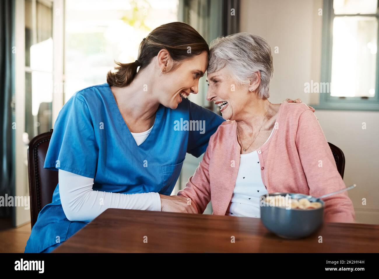 La felicità della sua paziente viene prima. Shot di una giovane infermiera seduta con una donna anziana a colazione in una casa di cura. Foto Stock