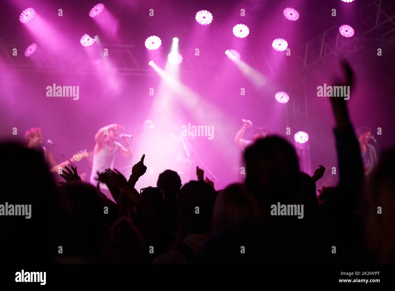 Una notte che non dimenticheranno mai. Vista posteriore di un pubblico con le mani alzate in un festival musicale e luci che fluiscono dall'alto del palco. Foto Stock