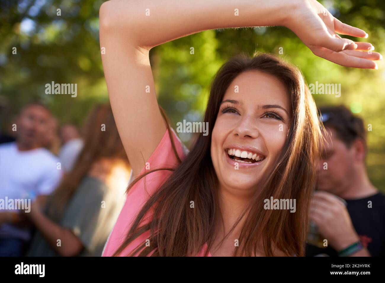 Divertimento. Una bella giovane donna sorridente e godendo di musica in un festival con braccio sollevato in aria e folla in background. Foto Stock