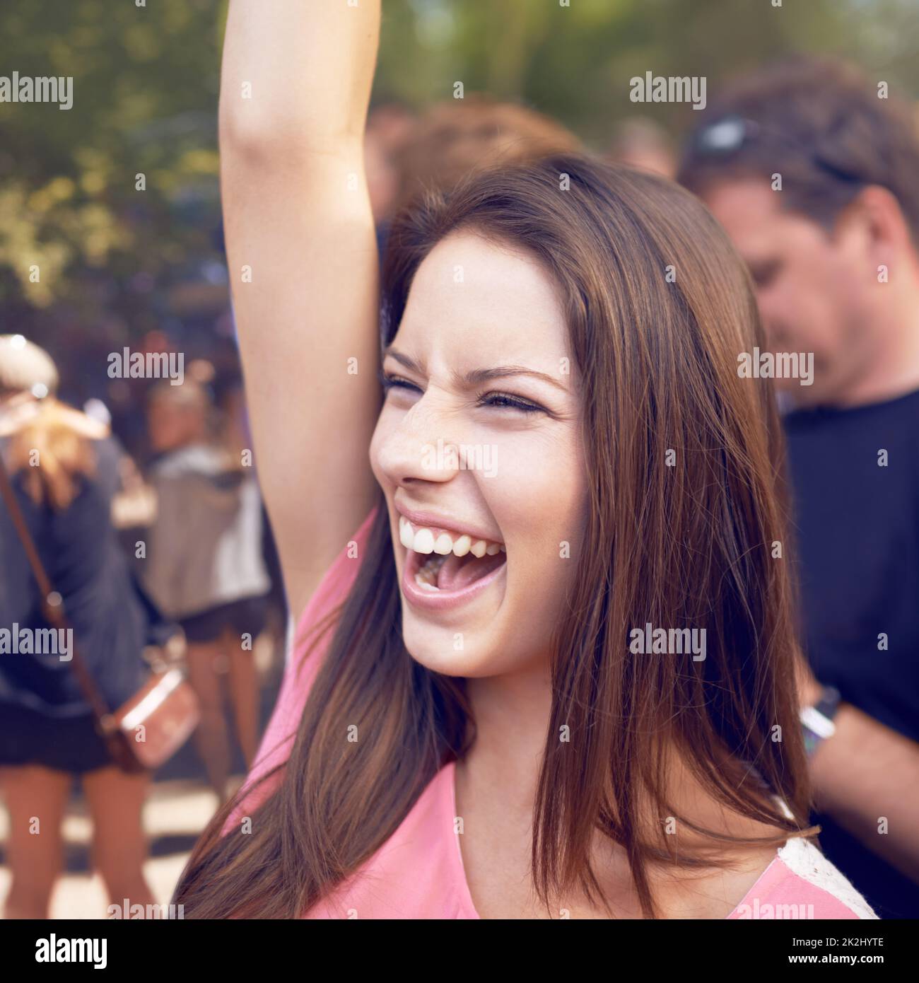 Whoohoo. Una bella giovane donna sorridente e godendo di musica in un festival con braccio sollevato in aria e folla in background. Foto Stock