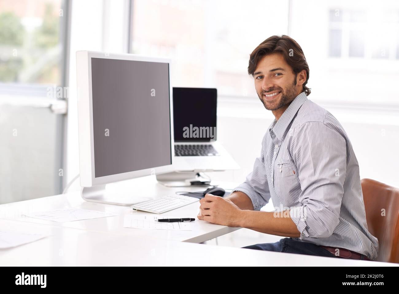 Questo è facile. Un giovane uomo d'affari seduto alla sua scrivania e sorridente alla macchina fotografica. Foto Stock
