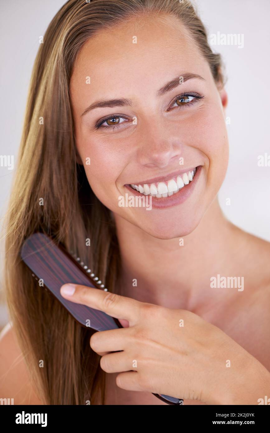 Il sorriso di una regina di bellezza. Una splendida donna brunetta spazzolando i suoi capelli lunghi sani. Foto Stock