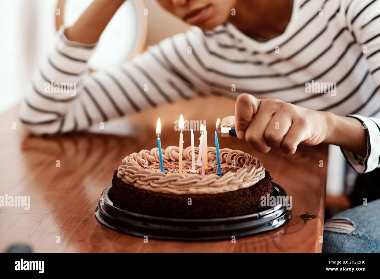 Compleanni in quarantine...not fresco. Scatto corto di una donna che illumina le candele su una torta di compleanno a casa e sembra triste. Foto Stock
