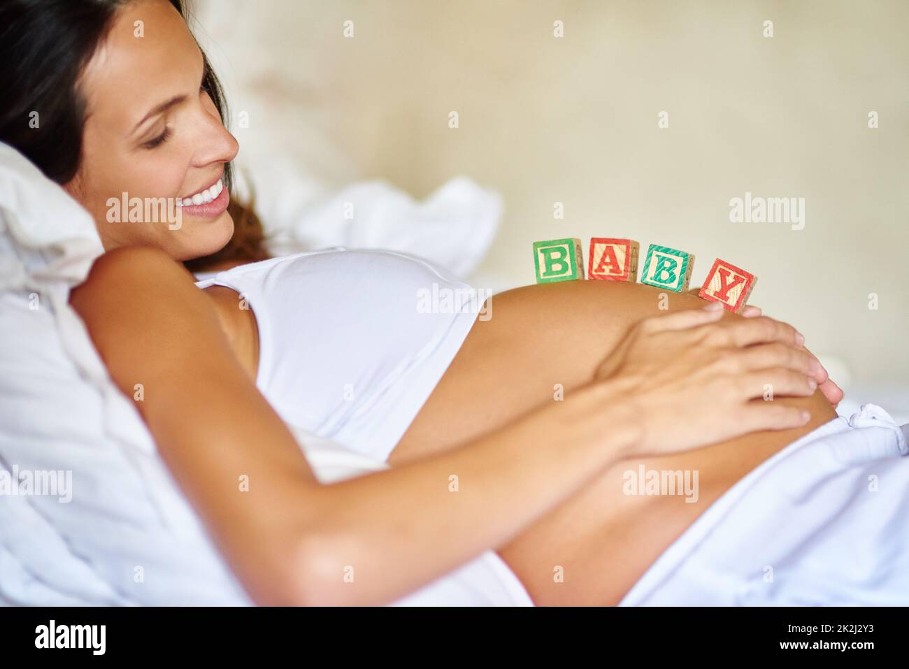 Non può aspettare di essere una mamma. Shot di una donna incinta sdraiata con blocchi di legno sul ventre. Foto Stock