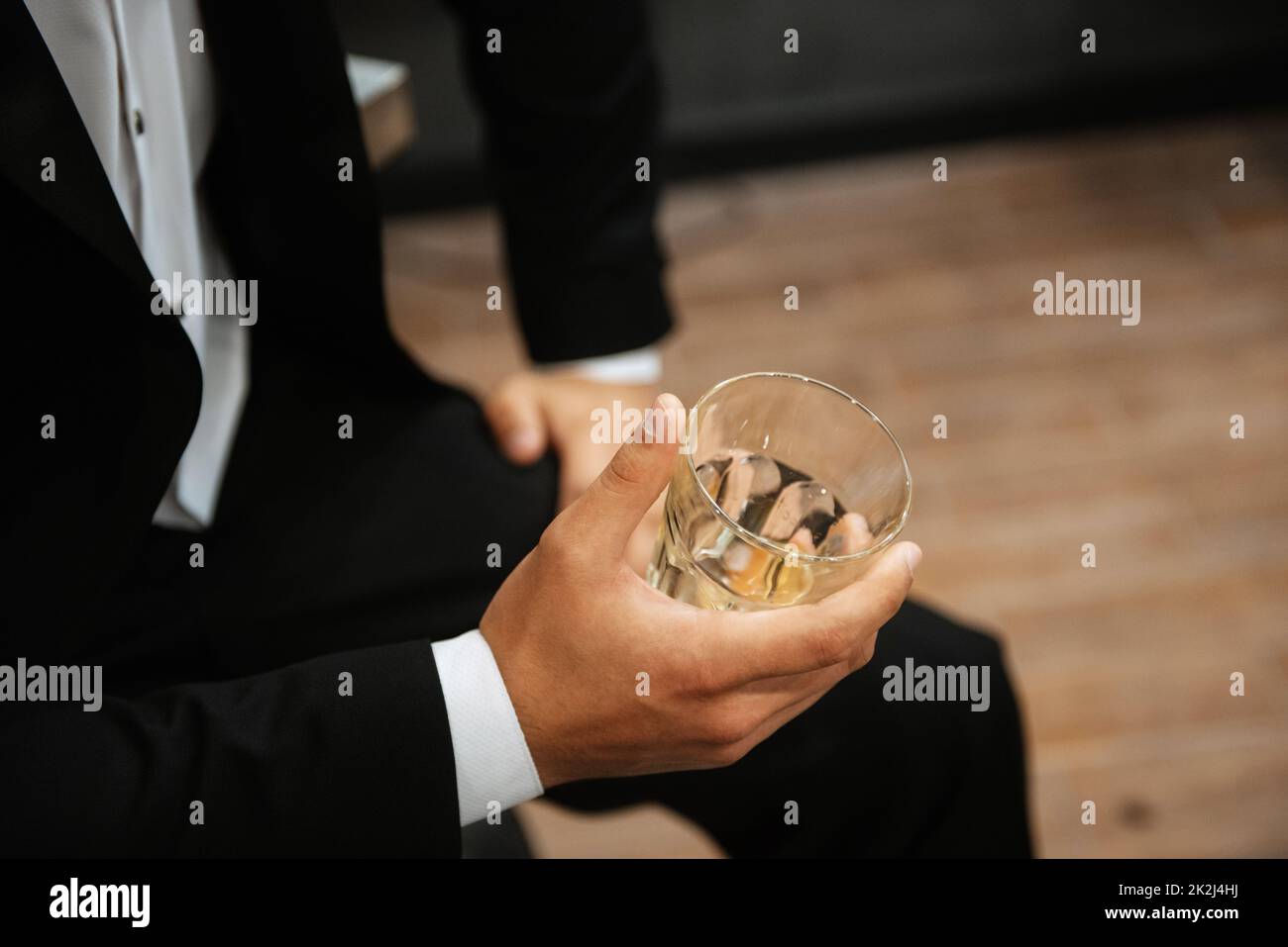 un bicchiere di whiskey in mano a un uomo in abito nero Foto Stock