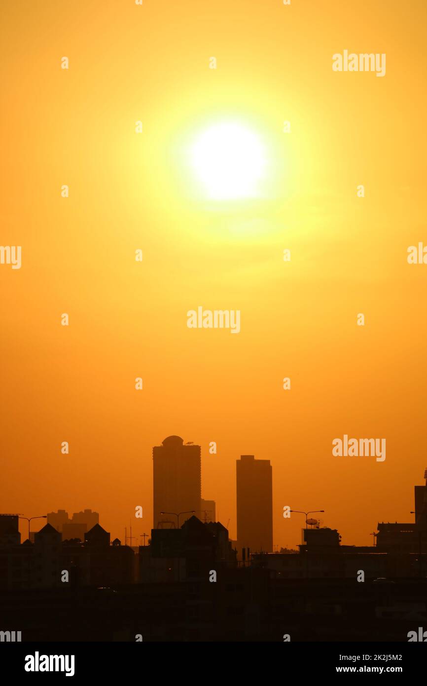 Sole luminoso che splende su un cielo arancione vivo su gruppi di grattacieli Foto Stock
