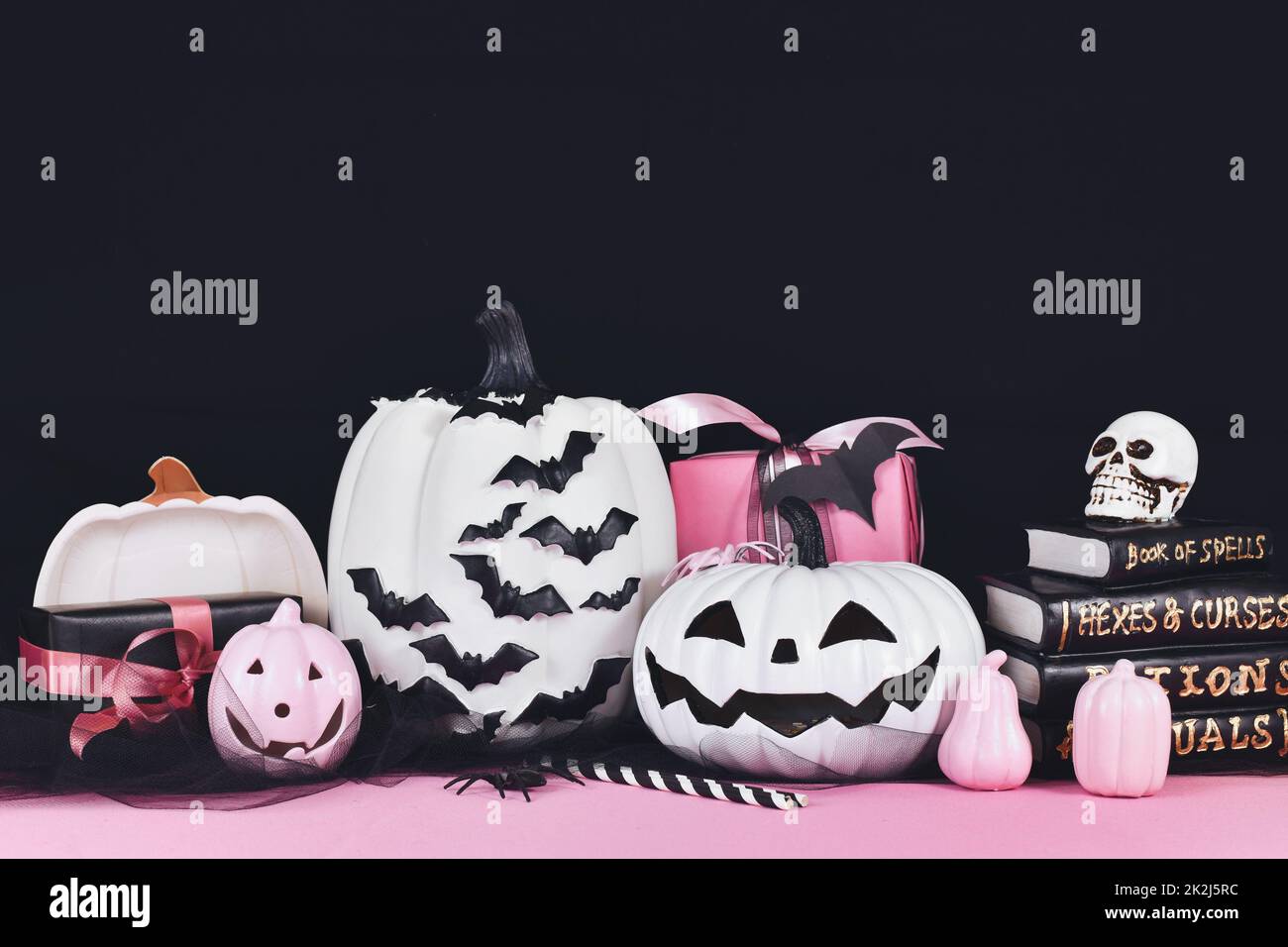 Decorazioni di Halloween rosa e bianco con zucche bianche e nere, libri di magia e ragni su sfondo nero con spazio copia Foto Stock
