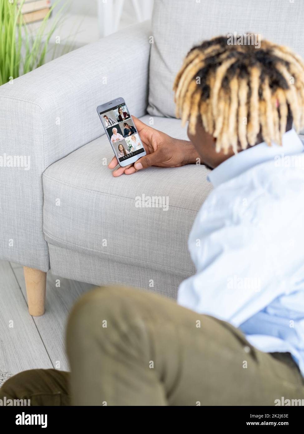 Videochiamata di gruppo. Lavoro remoto. Telelavoro WFH. Libero professionista maschile rilassato utilizzando il telefono sul divano per cooperare con il team aziendale online da casa. Foto Stock
