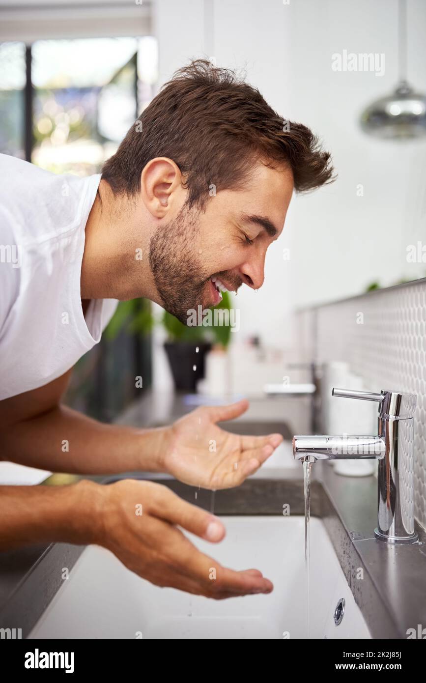 La sensazione rinfrescante di un viso pulito. Primo piano di un bell'uomo che lava il viso in bagno a casa. Foto Stock