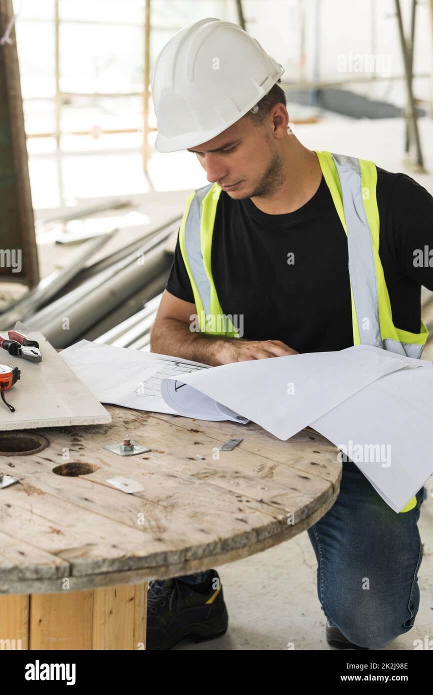 Il lavoratore sta controllando i progetti durante il suo lavoro su una costruzione Foto Stock