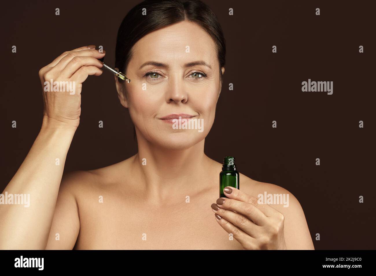 Bella donna di mezza età in bottiglia con olio cosmetico o siero per la sua pelle Foto Stock