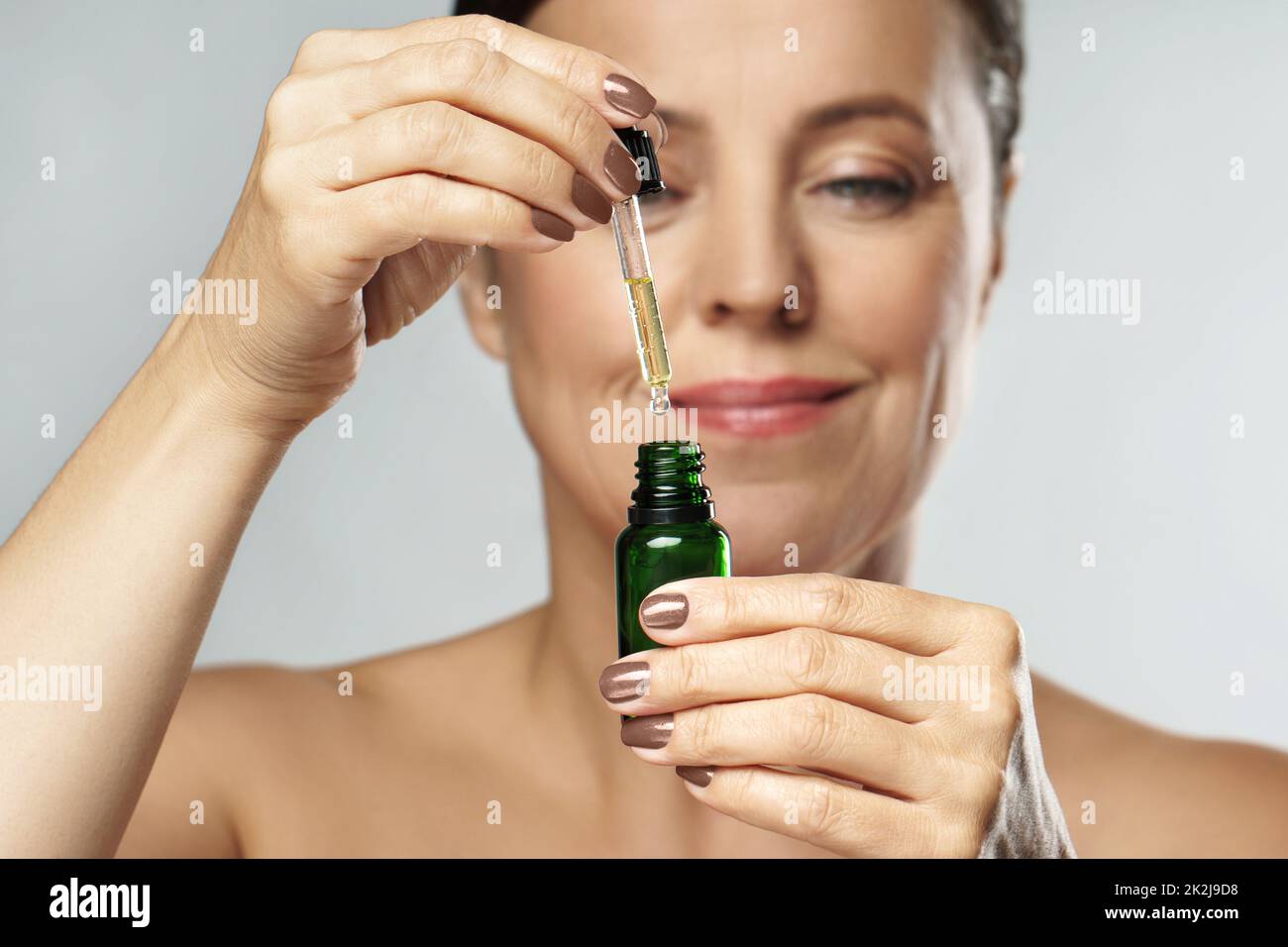 Bella donna di mezza età in bottiglia con olio cosmetico o siero per la sua pelle Foto Stock