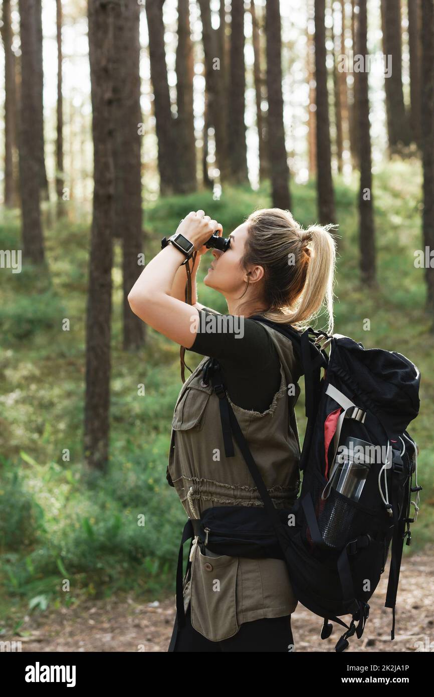 L'escursionista femminile utilizza il binocolo per il bird watching nella foresta verde Foto Stock