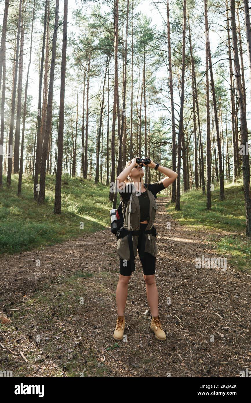 L'escursionista femminile utilizza il binocolo per il bird watching nella foresta verde Foto Stock