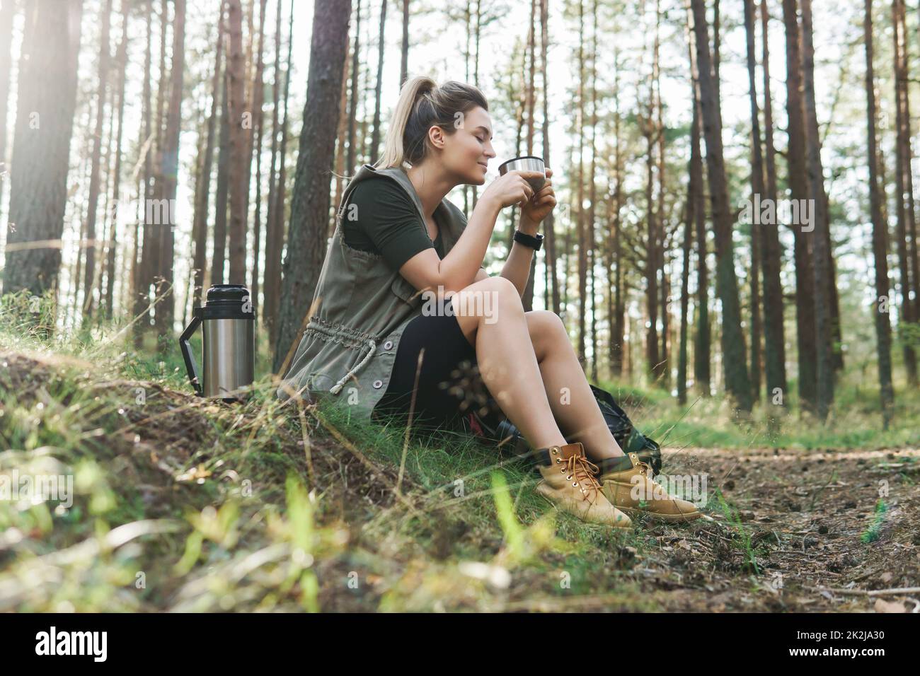 Escursionista durante la piccola sosta con un pallone vuoto bere caffè caldo o tè nella foresta verde Foto Stock