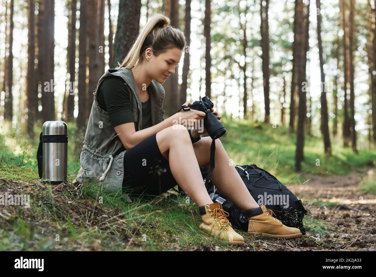 Escursionista seduto con moderna macchina fotografica mirrorless in verde foresta Foto Stock