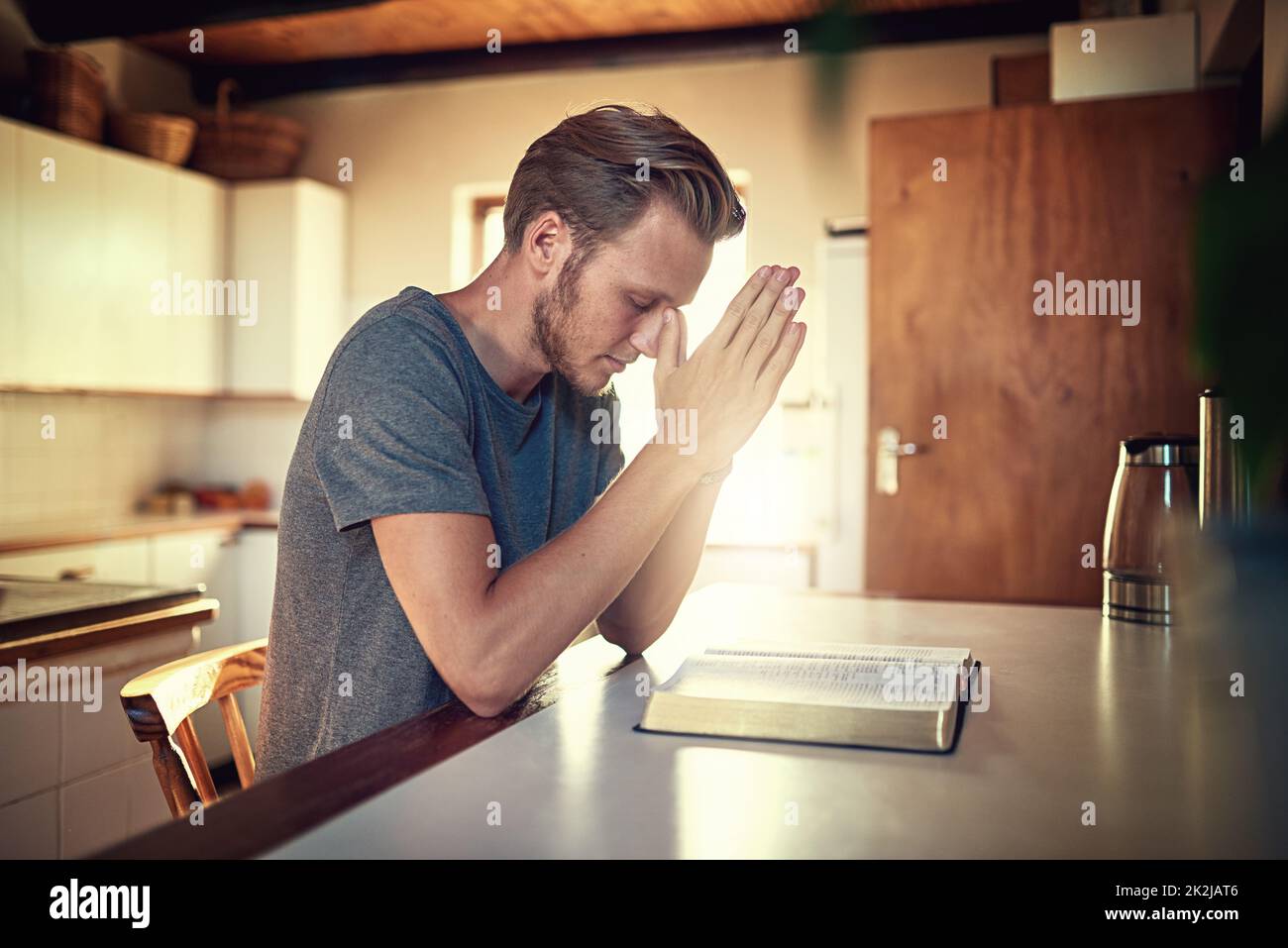 Attraverso le sue devozioni quotidiane. Scatto di un giovane devoto che stringe le mani in preghiera sopra una Bibbia aperta. Foto Stock