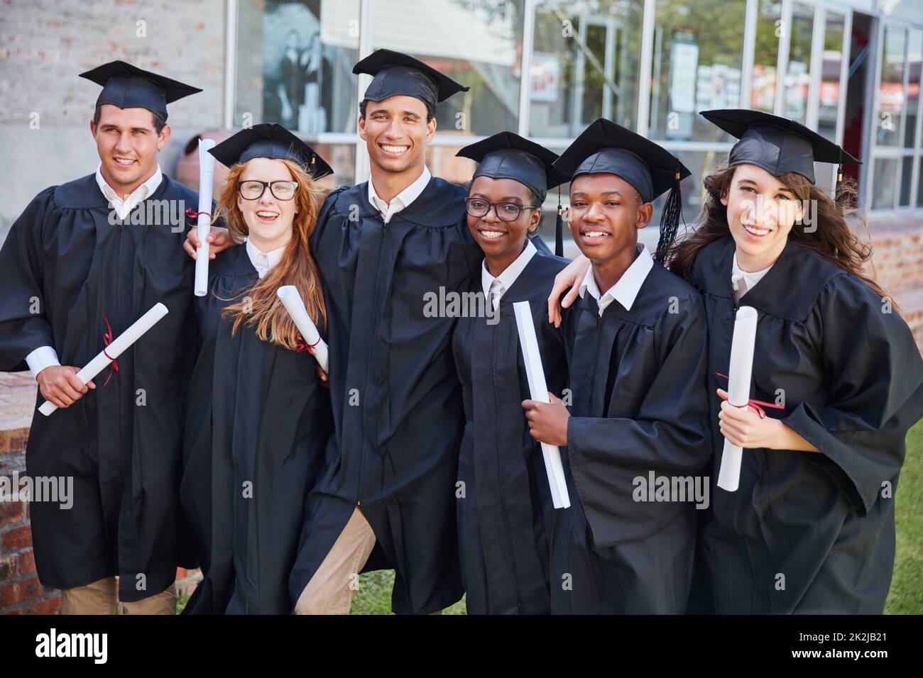 Ora possiamo chiamarci laureati. Ritratto di un felice gruppo di studenti che si levano in piedi fuori il giorno della laurea. Foto Stock