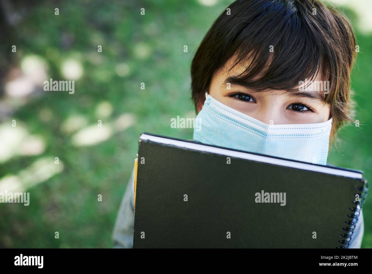 Due cose che non dovreste dimenticare mai. Scatto di un ragazzino che indossa una maschera e tiene libri in natura. Foto Stock