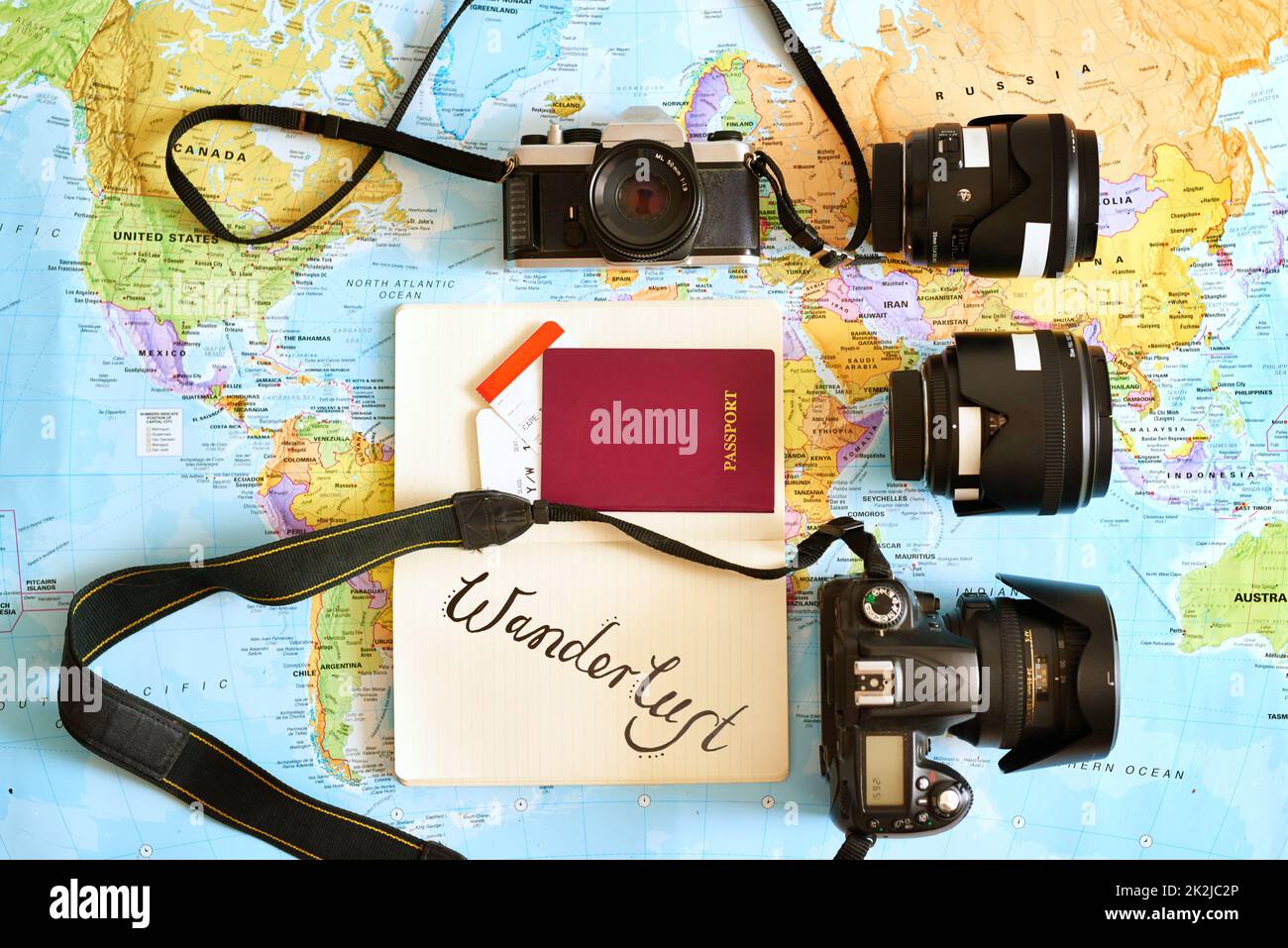 Non viaggiare mai senza la tua fotocamera preferita. Scatto ad angolo elevato di una mappa con passaporto e varie fotocamere e obiettivi disposti su di essa. Foto Stock